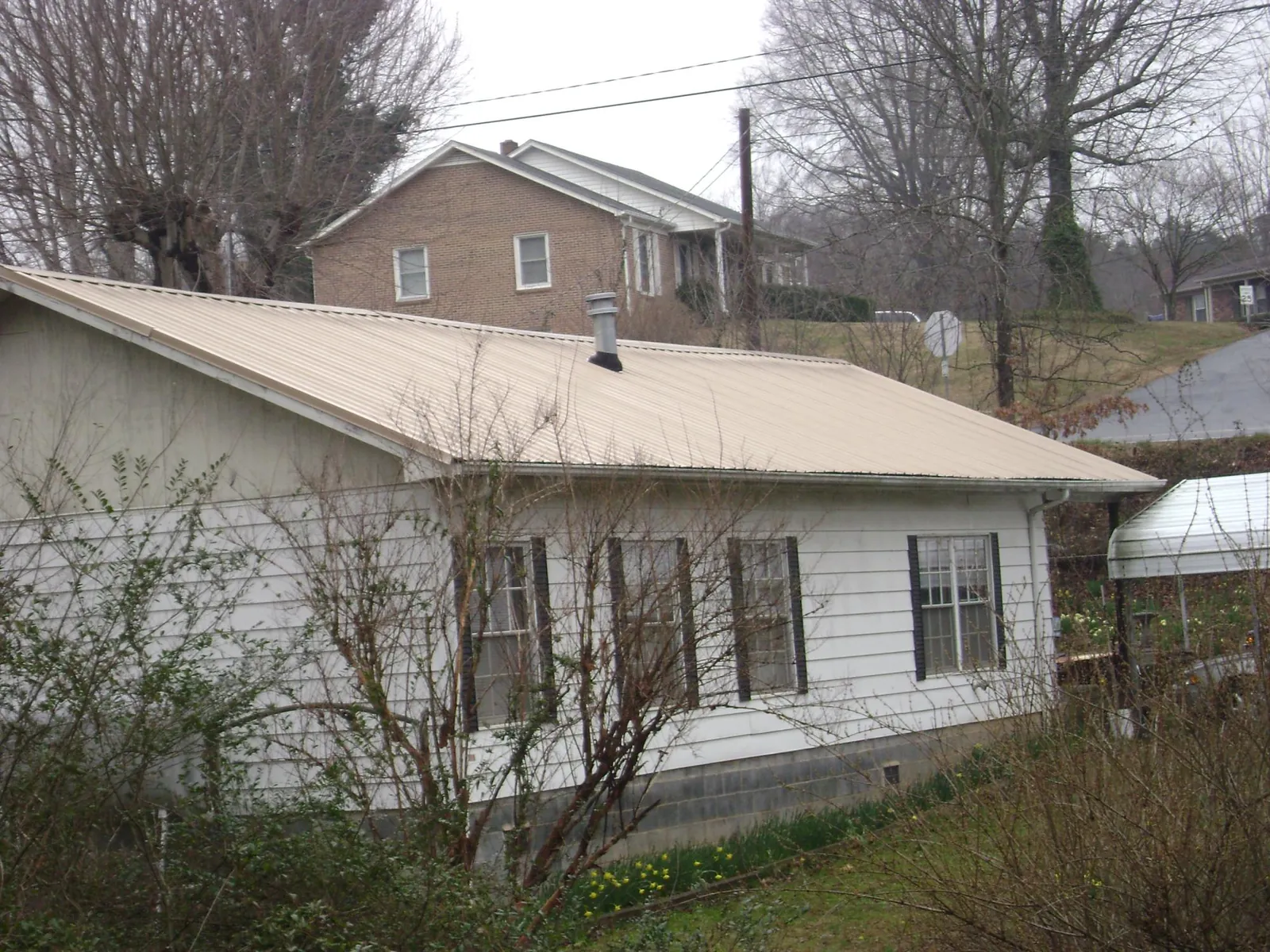 Tan metal roof on a white sided house set into a hillside — Commercial Roofing by Roofing Brothers in Garland